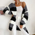 A woman wearing gray, black and white colorblock cardigan styled with white top and white pants against neutral backdrop
