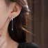 Crystal-encrusted bow earring with chain pendant shown on ear, capturing sparkle detail and manicured hand