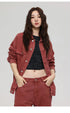 A woman with wavy hair poses in rust colored denim jacket over black cropped top showing midriff against white background