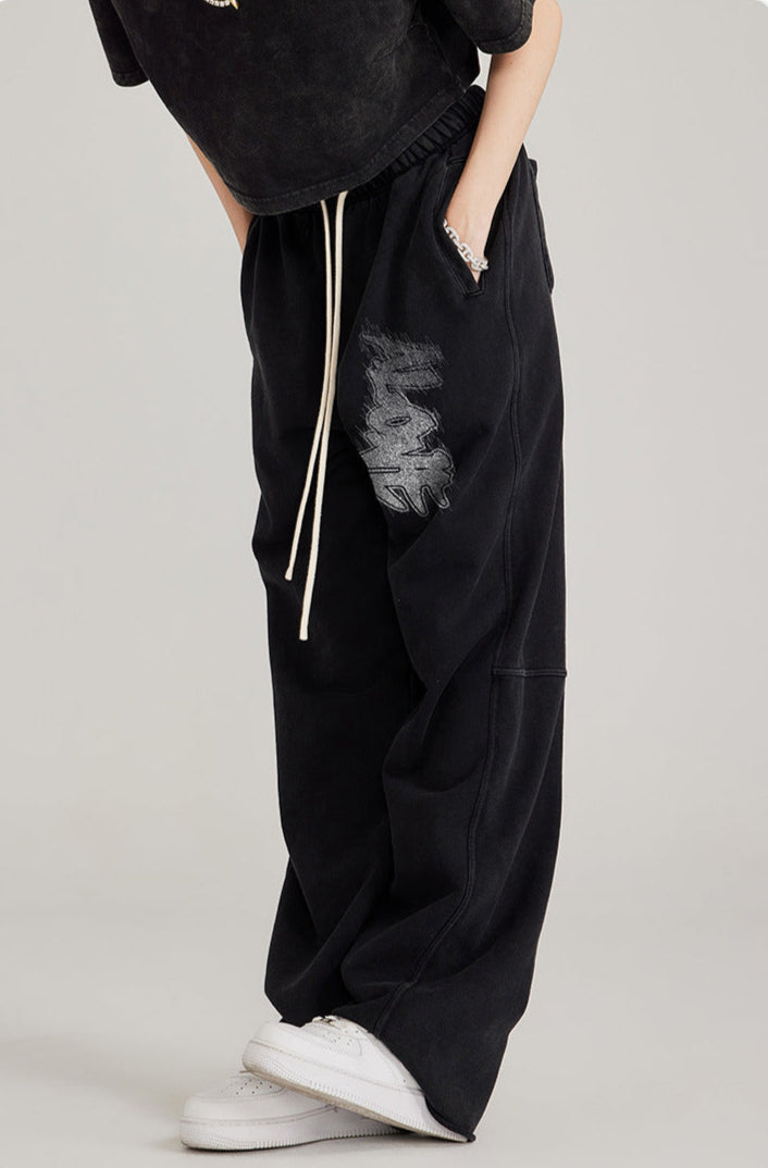 Side view of black sweatpants with white drawstring and graffiti detail. Styled with white Air Force 1 sneakers