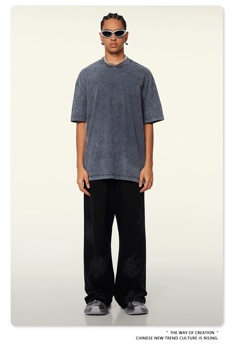 Model with dreadlocks wearing black oversized t-shirt with brown distressed jeans and black footwear against beige background