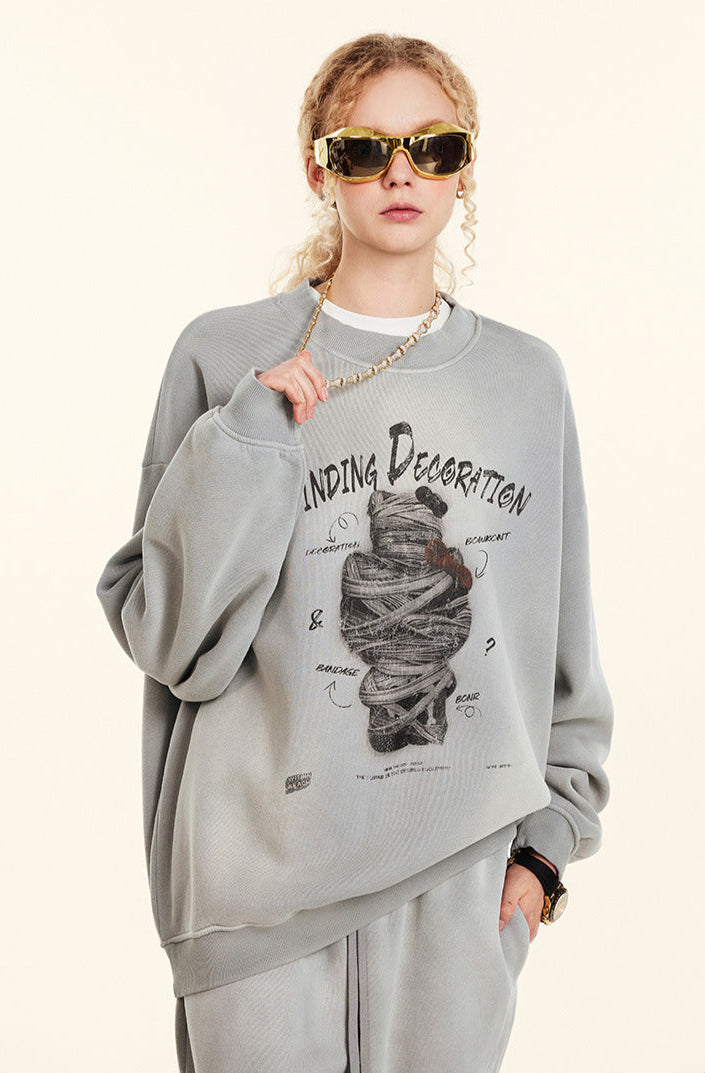 Close-up of female model wearing gray sweatshirt with Winding Decoration graphic, gold sunglasses, gold chain, hand touching necklace, profile angle