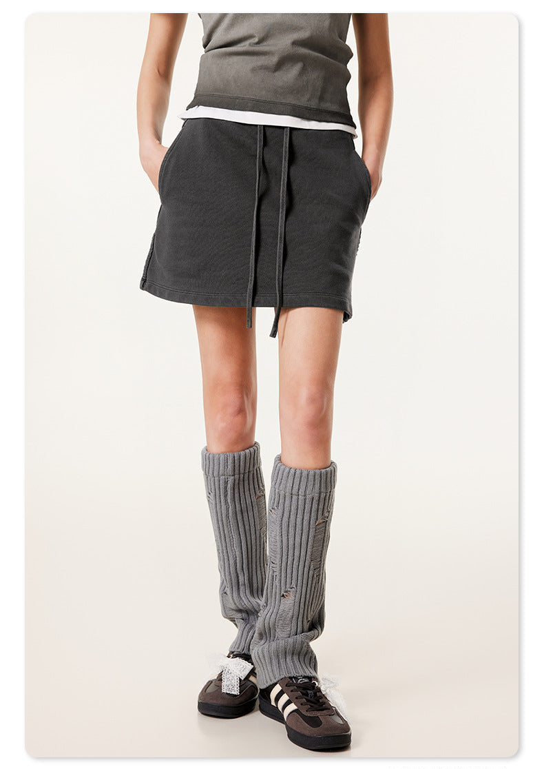 Close-up of black mini skirt on model showing side pocket detail and paired with gray ribbed leg warmers