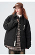Model with auburn curls wearing black ASTROSMASH puffer jacket over plaid shirt with brown cap and wide-leg pants