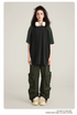Model with curly dark hair wearing black and olive cargo pants with zippered pouches, oversized black/olive t-shirt, white headphones and cream sneakers on neutral background