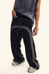 Model in dark navy t-shirt wearing black denim track pants with gray side stripes, styled with athletic footwear in studio setting