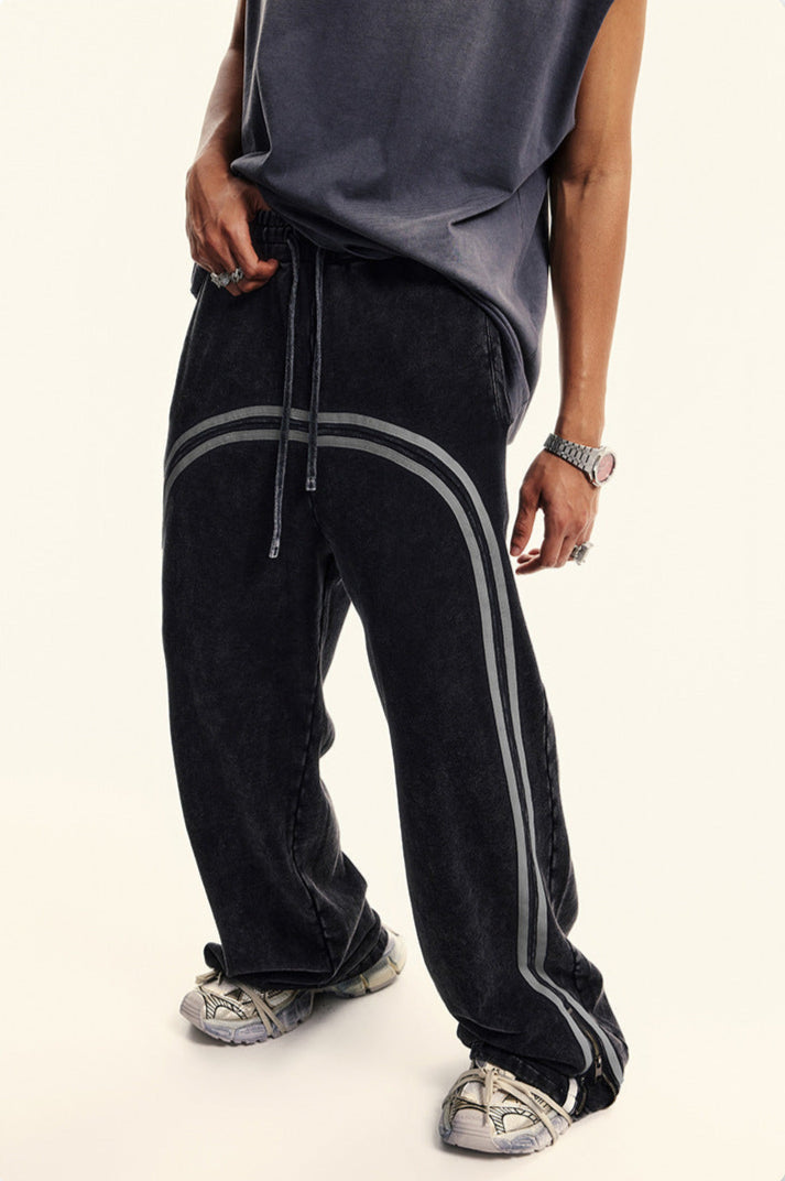 Model in dark navy t-shirt wearing black denim track pants with gray side stripes, styled with athletic footwear in studio setting
