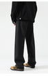 Black wide-leg jeans with relaxed fit, shown with jacket hem and tan suede sneakers