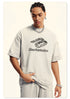Close-up of model in cream Backstairs t-shirt with distressed logo print, silver chain necklace, hand in pocket against white backdrop