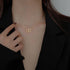 Gold chain necklace with intertwined heart-shaped pendant, worn close to a black-clothed shoulder