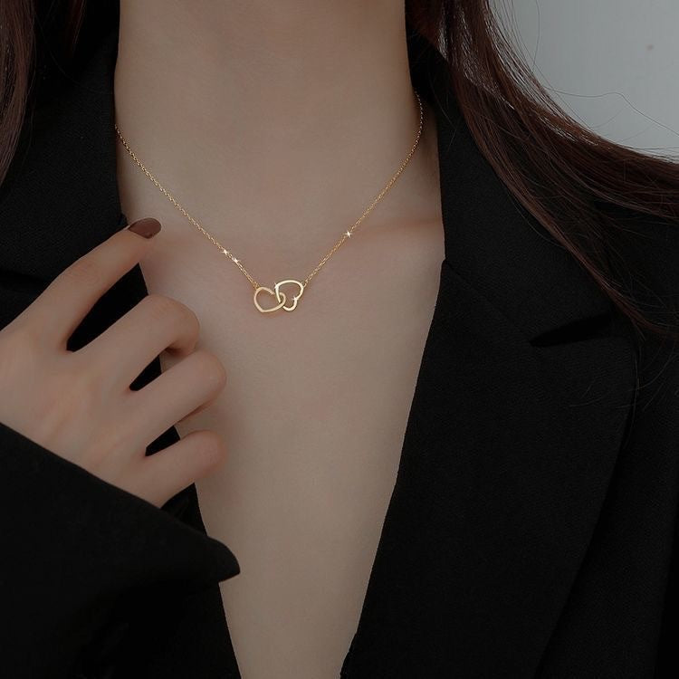 Gold chain necklace with intertwined heart-shaped pendant, worn close to a black-clothed shoulder