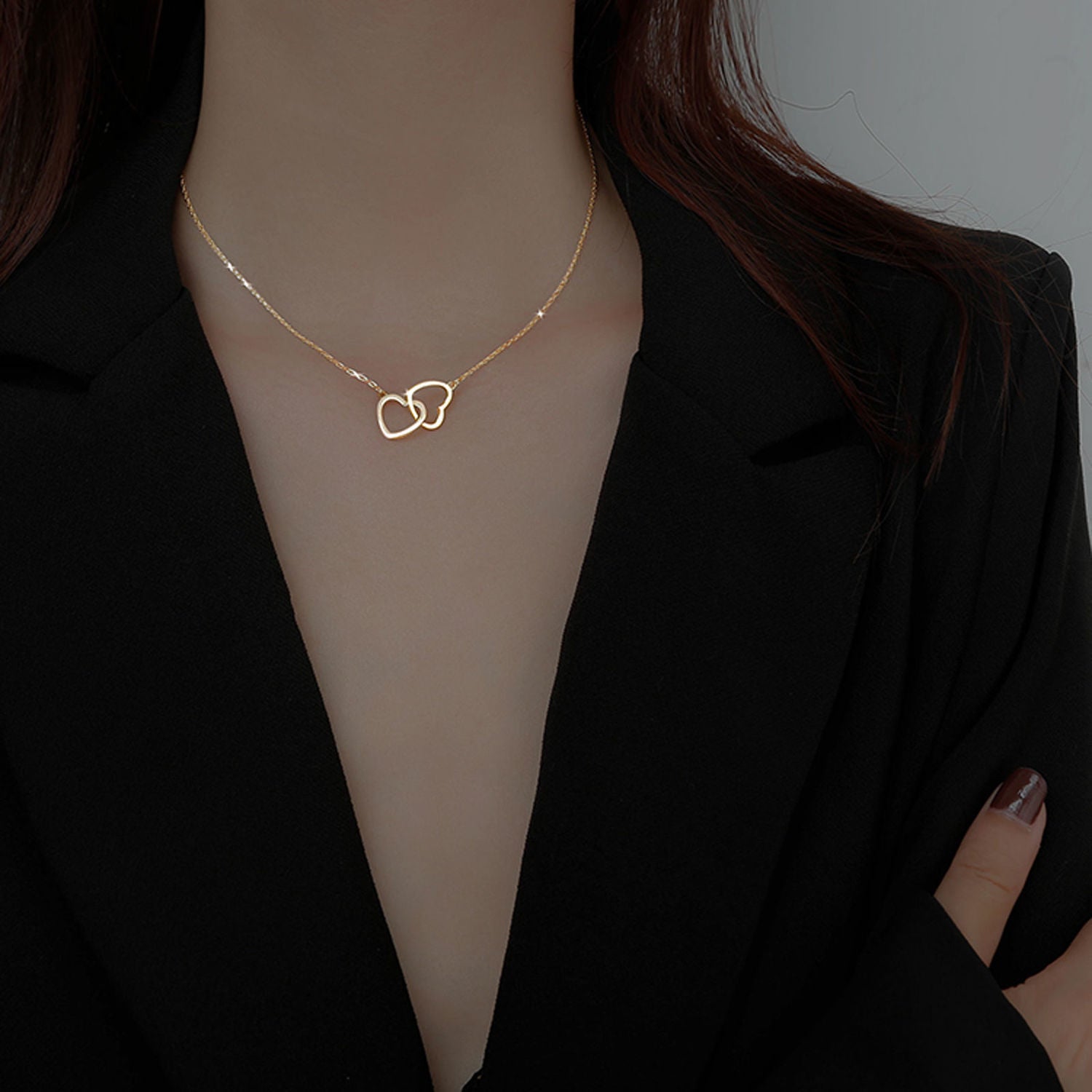 Gold chain necklace with interconnected heart-shaped pendant, worn against a black backdrop