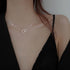 Silver chain necklace with interlocking heart-shaped pendant, worn close to a black-clothed shoulder