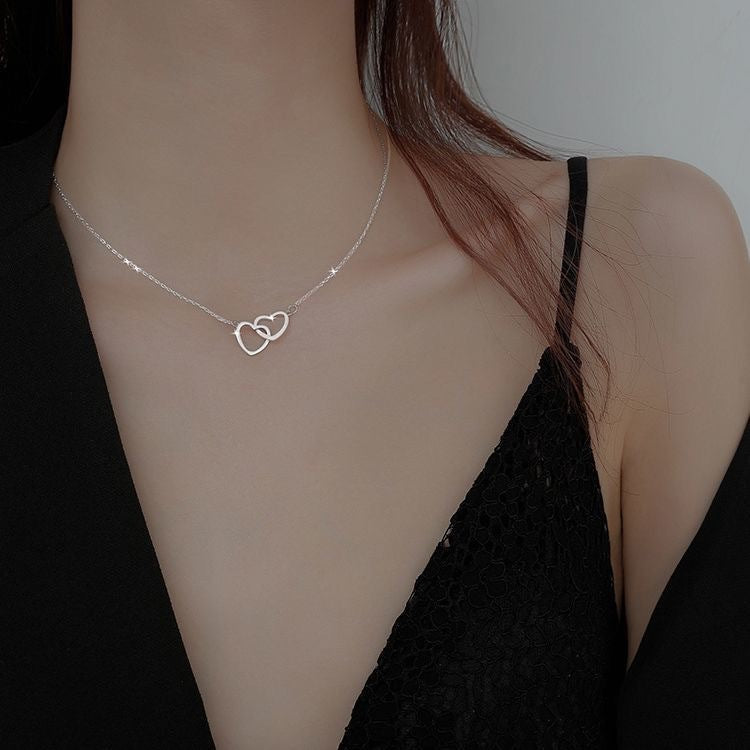 Silver chain necklace with interlocking heart-shaped pendant, worn close to a black-clothed shoulder