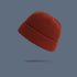 A rust orange ribbed knit beanie with folded cuff floating against slate gray background, showing warm autumn-toned winter hat