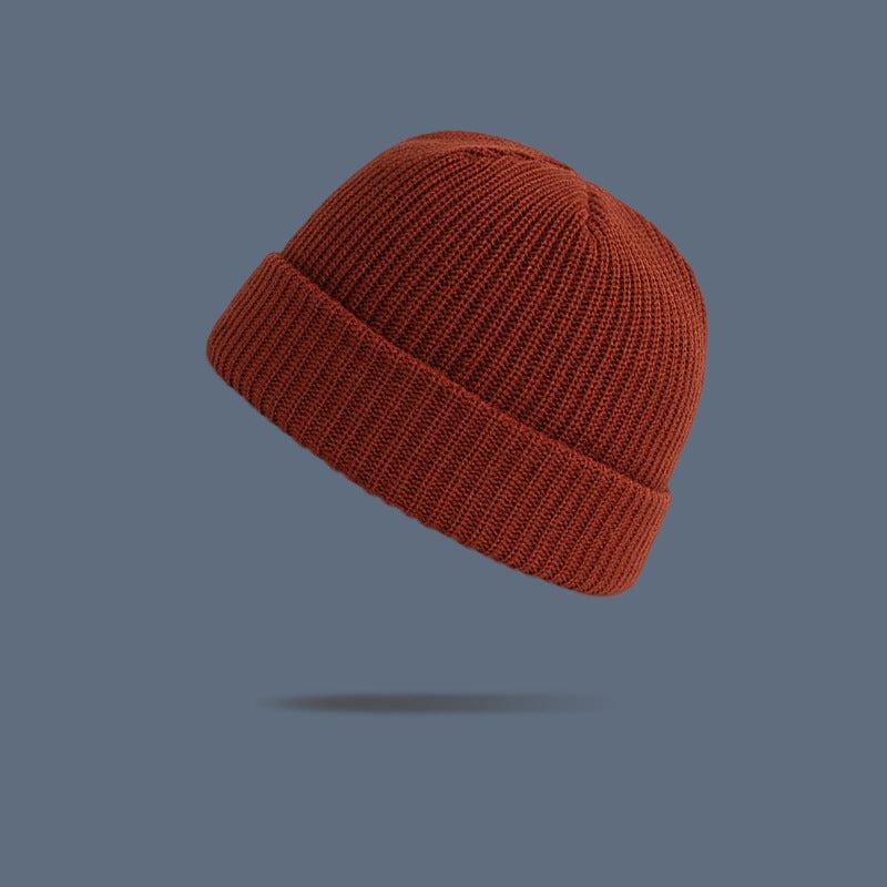 A rust orange ribbed knit beanie with folded cuff floating against slate gray background, showing warm autumn-toned winter hat