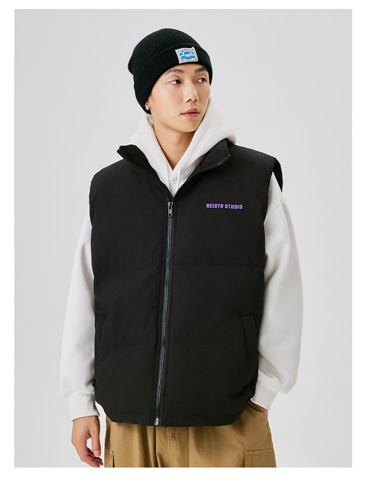 Man in black puffer vest over white hoodie with black beanie, showing contrast layering style against white background