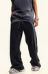 Close-up of black denim track pants with light gray double stripes down legs, showing stretch waistband with drawstring detail