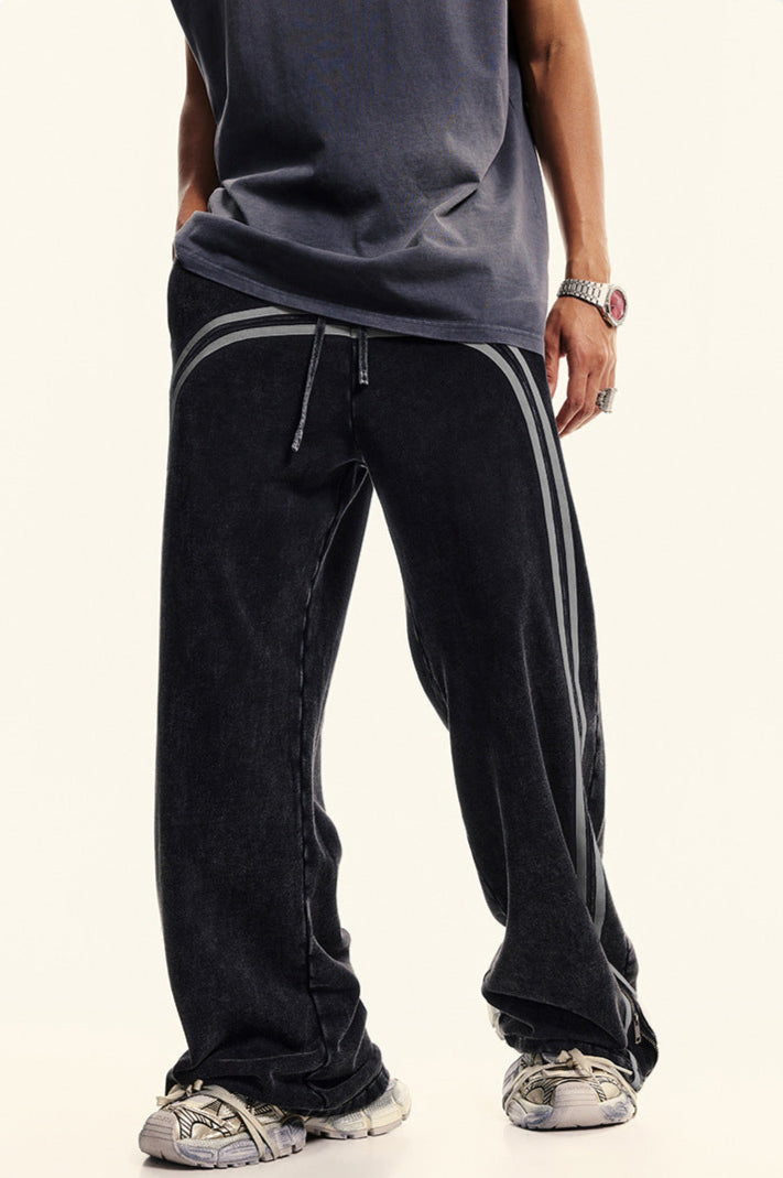 Close-up of black denim track pants with light gray double stripes down legs, showing stretch waistband with drawstring detail