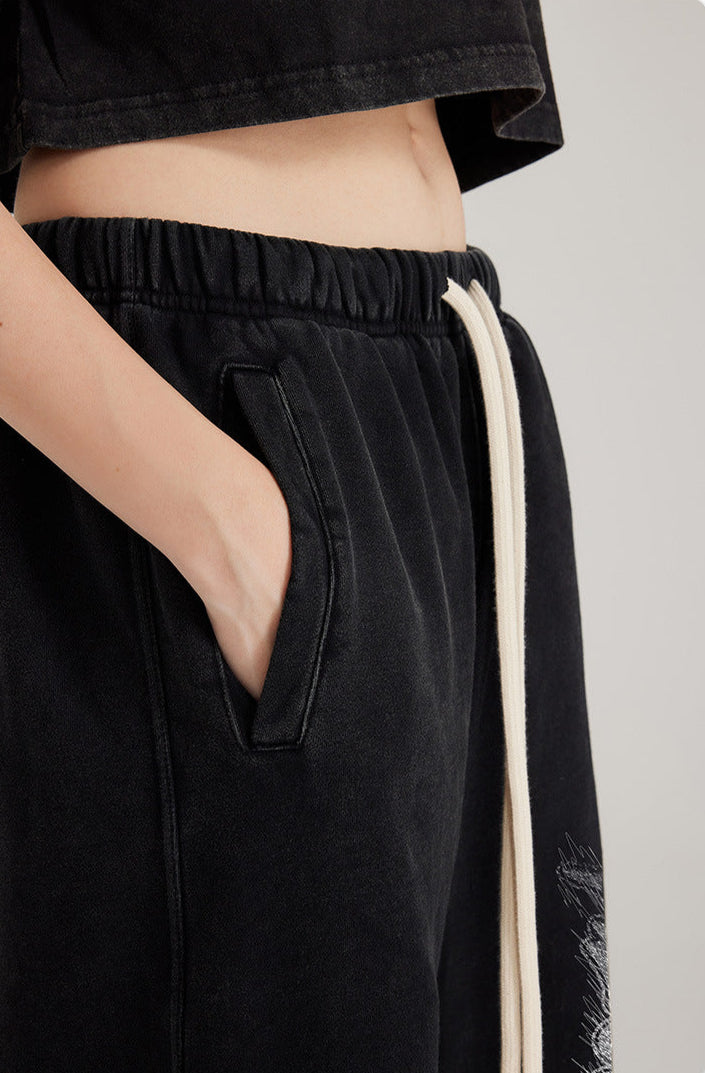 Close-up of black sweatpants pocket detail with hand showing white drawstring and contrasting graphic print