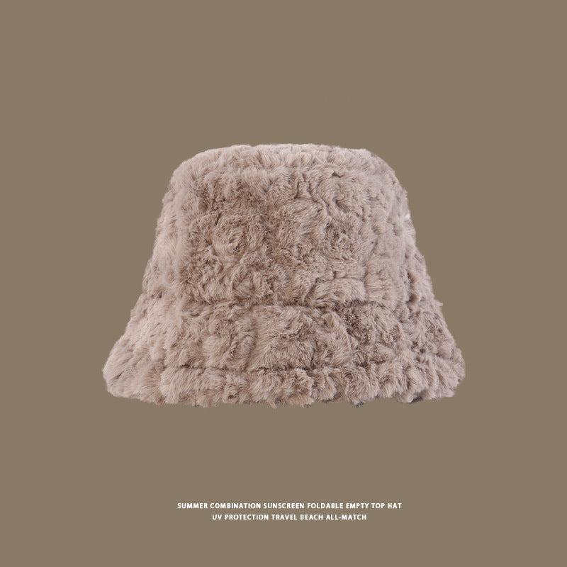 Close-up of a beige faux fur bucket hat with a soft, fluffy texture against a brown background
