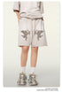 Beige cotton shorts with embroidered cupid graphics, paired with matching oversized tee and vintage-style sneakers
