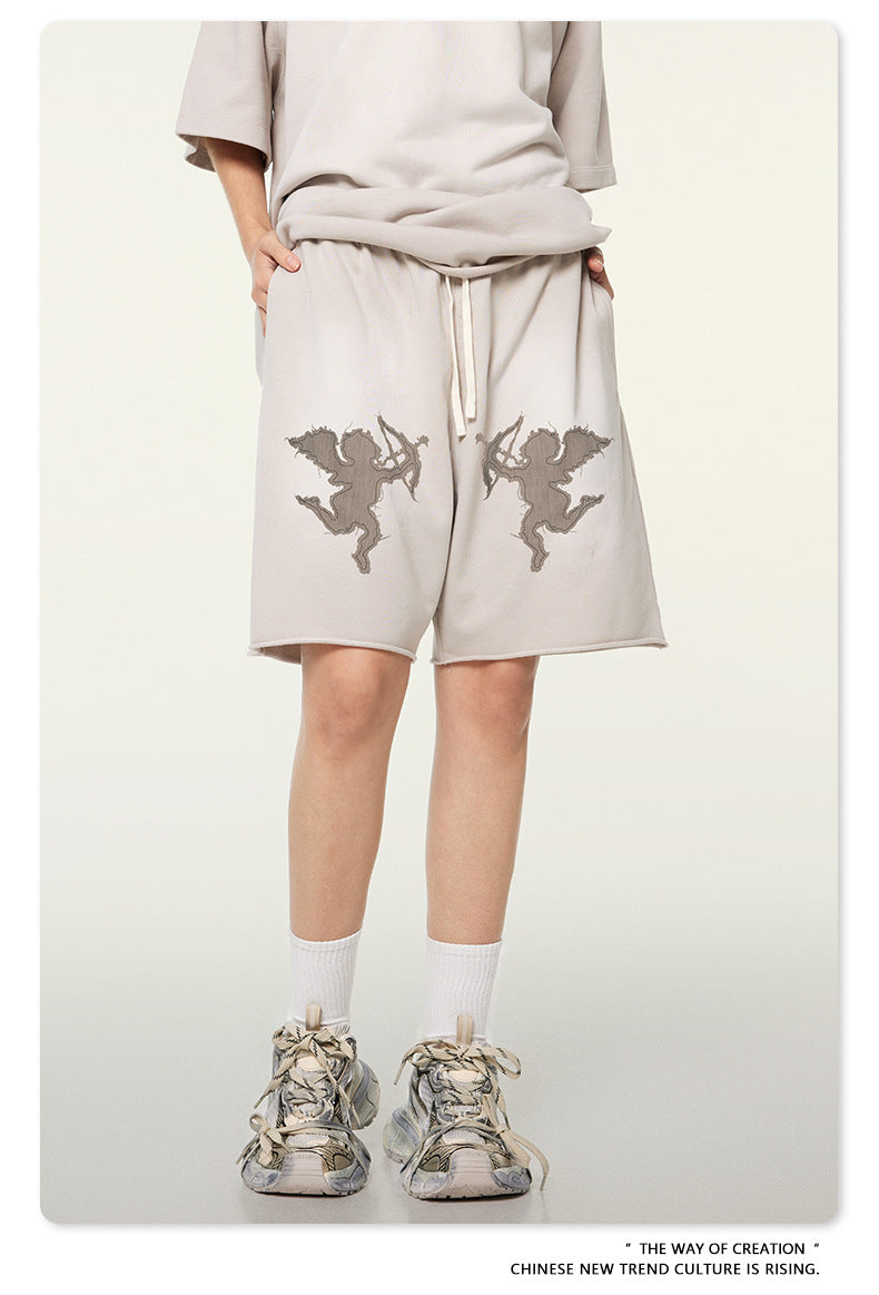 Beige cotton shorts with embroidered cupid graphics, paired with matching oversized tee and vintage-style sneakers