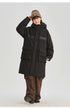 A woman wearing brown beanie adjusts her hat while modeling black NEIGHBORHOOD parka with brown pants against white background