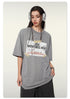 Woman wearing gray oversized t-shirt with 'NEW ADVENTURES AHEAD' graphic, silver headphones, and wide-leg shorts