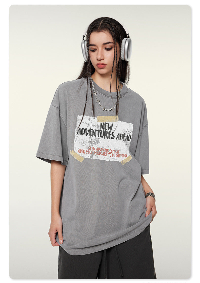 Woman wearing gray oversized t-shirt with 'NEW ADVENTURES AHEAD' graphic, silver headphones, and wide-leg shorts