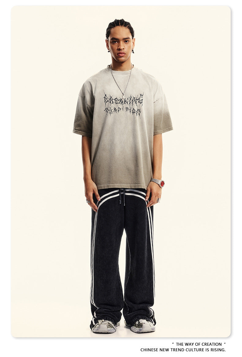 Breaking Tradition oversized gray tee with gothic text design, styled with black trackpants and silver chain necklace