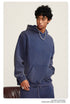 Young man in navy pullover hoodie with silver chain necklace against neutral backdrop