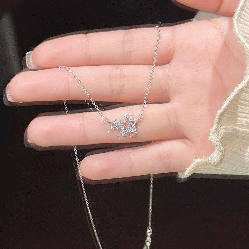 A woman is holding a silver double star pendant necklace in her palm, showing French manicure tips against a dark background