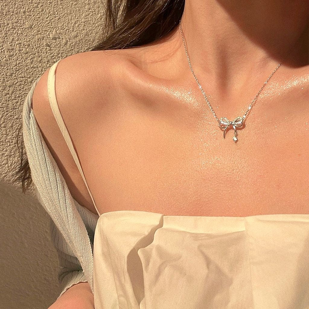 Silver bow necklace with crystals worn with cream off-shoulder top in sunlight