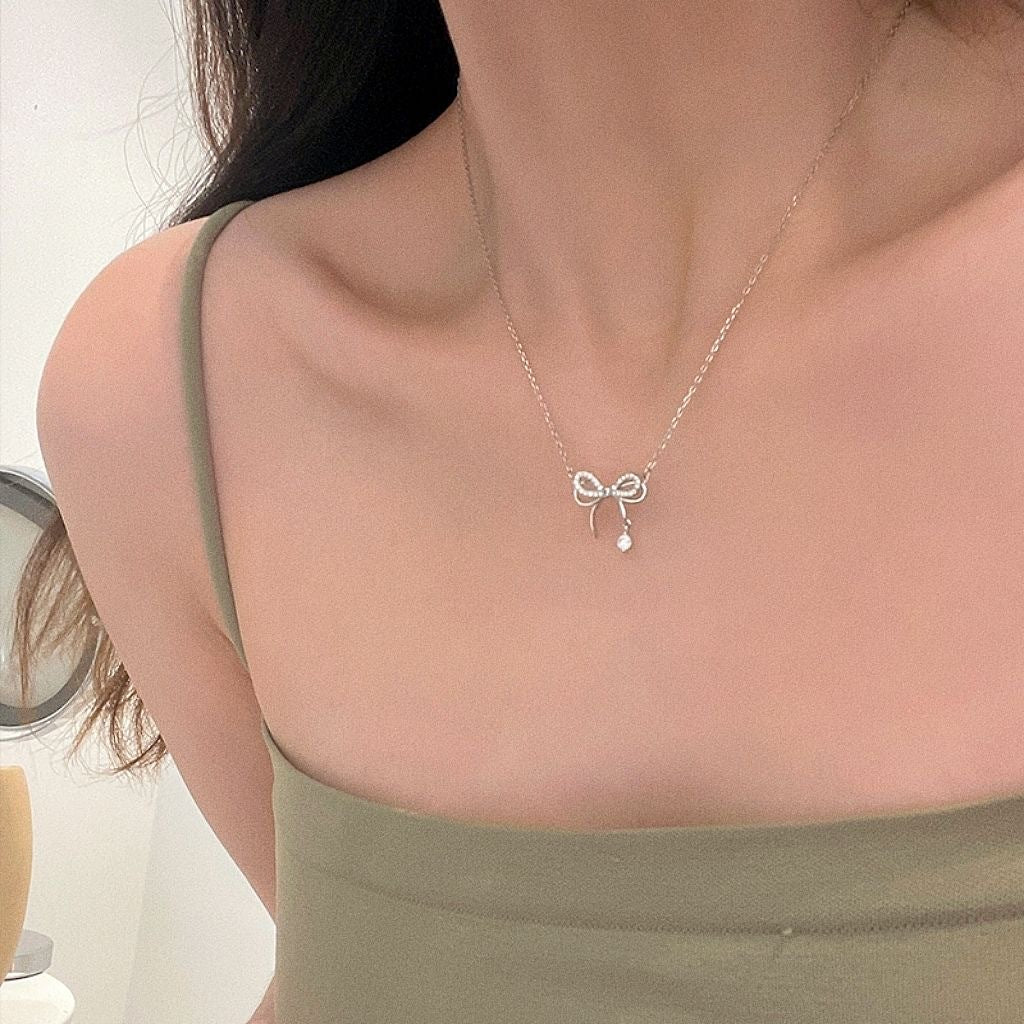 Delicate silver bow necklace with crystal pendant worn with olive green top