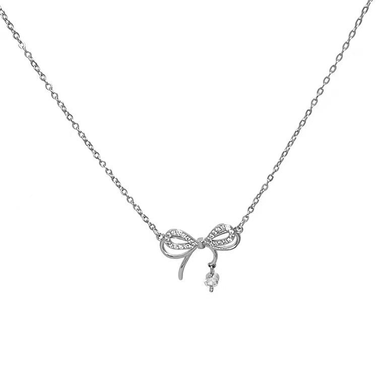 Product photo of silver necklace featuring crystal-adorned bow and dangling pearl charm on white background