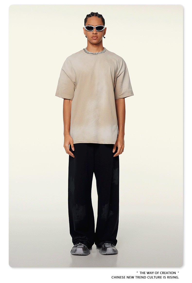 Model with braided hair wearing beige t-shirt, black wide-leg pants, white sunglasses and silver chain necklace against cream background