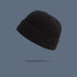 A black ribbed knit beanie with folded cuff floating against slate gray background, showing warm autumn-toned winter hat