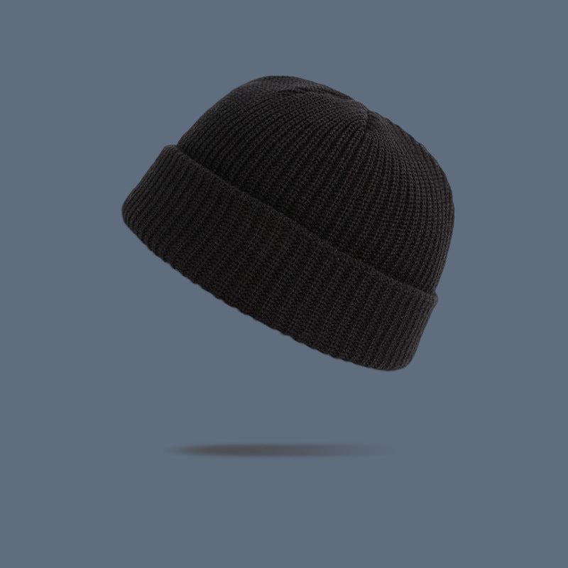 A black ribbed knit beanie with folded cuff floating against slate gray background, showing warm autumn-toned winter hat