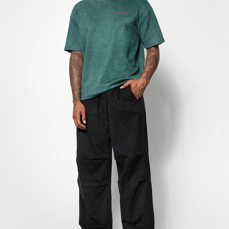 A male model wears a green oversized T-shirt, black wide-leg pants, and black-and-white sneakers, standing against a white background