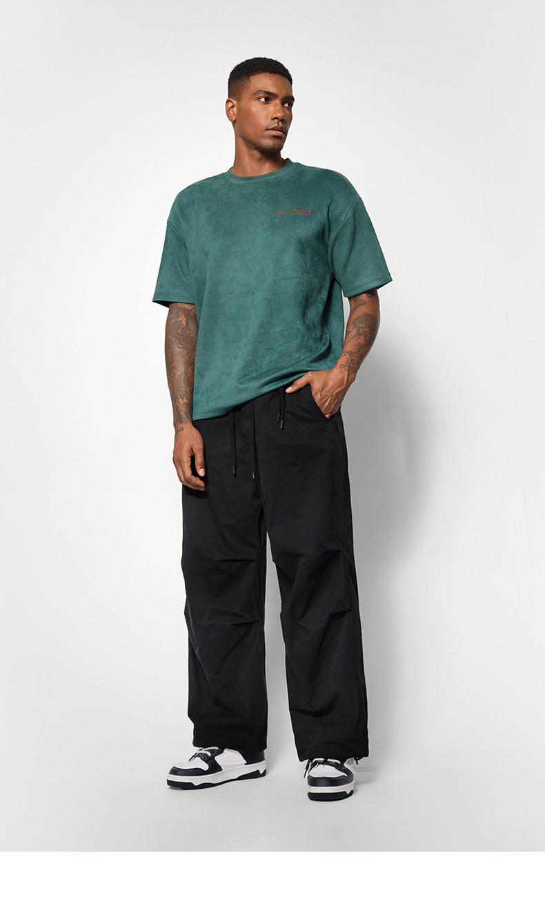 A male model wears a green oversized T-shirt, black wide-leg pants, and black-and-white sneakers, standing against a white background
