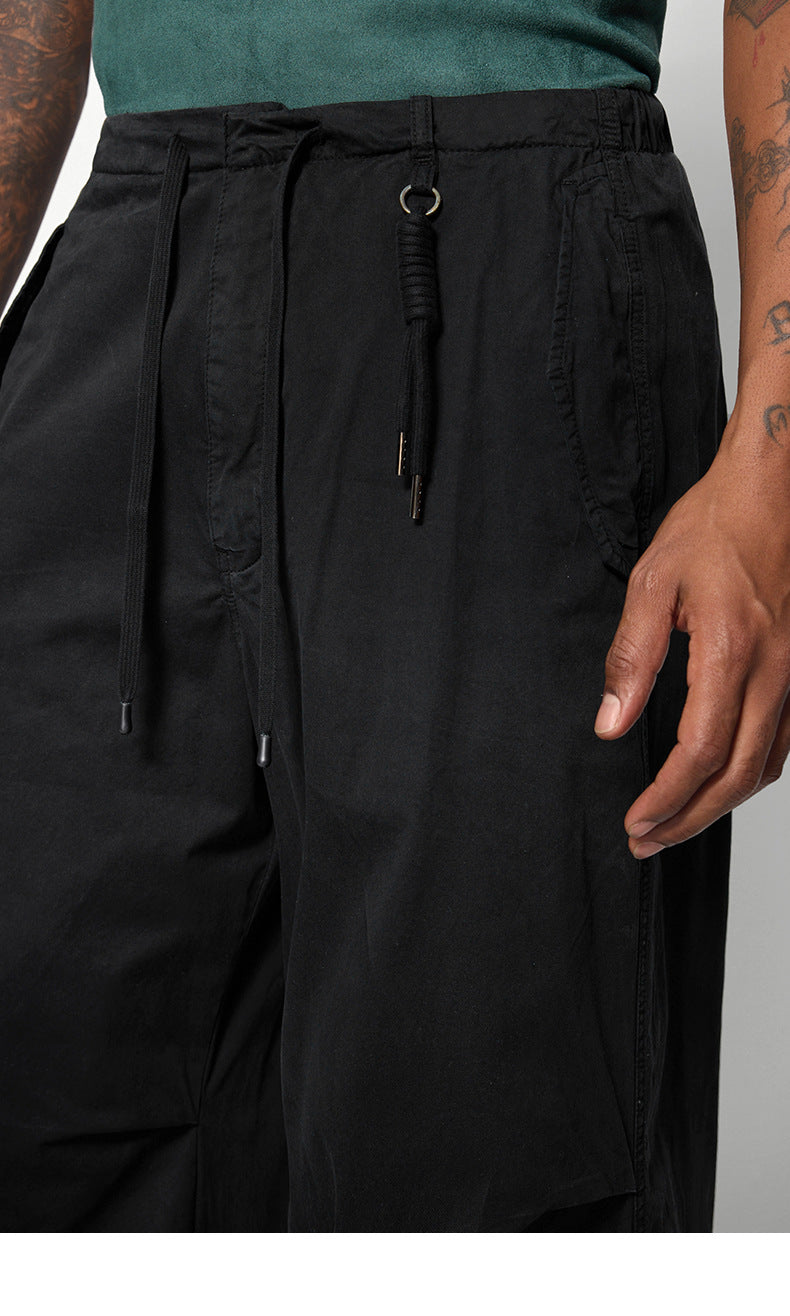 A close-up of black drawstring pants with a decorative knot and ring detail, highlighting the waistband and pocket