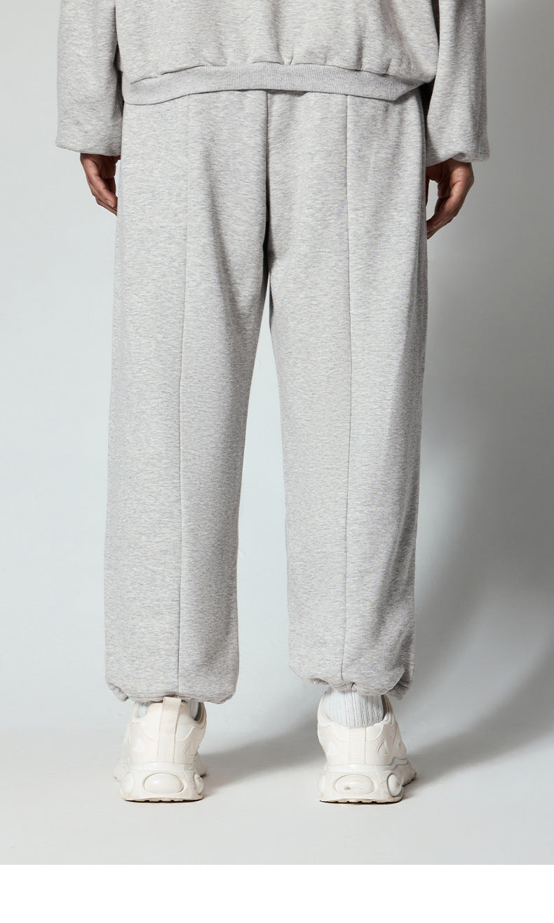 Detailed view of light gray sweatpants with center seam and elasticated bottom, showcasing relaxed fit