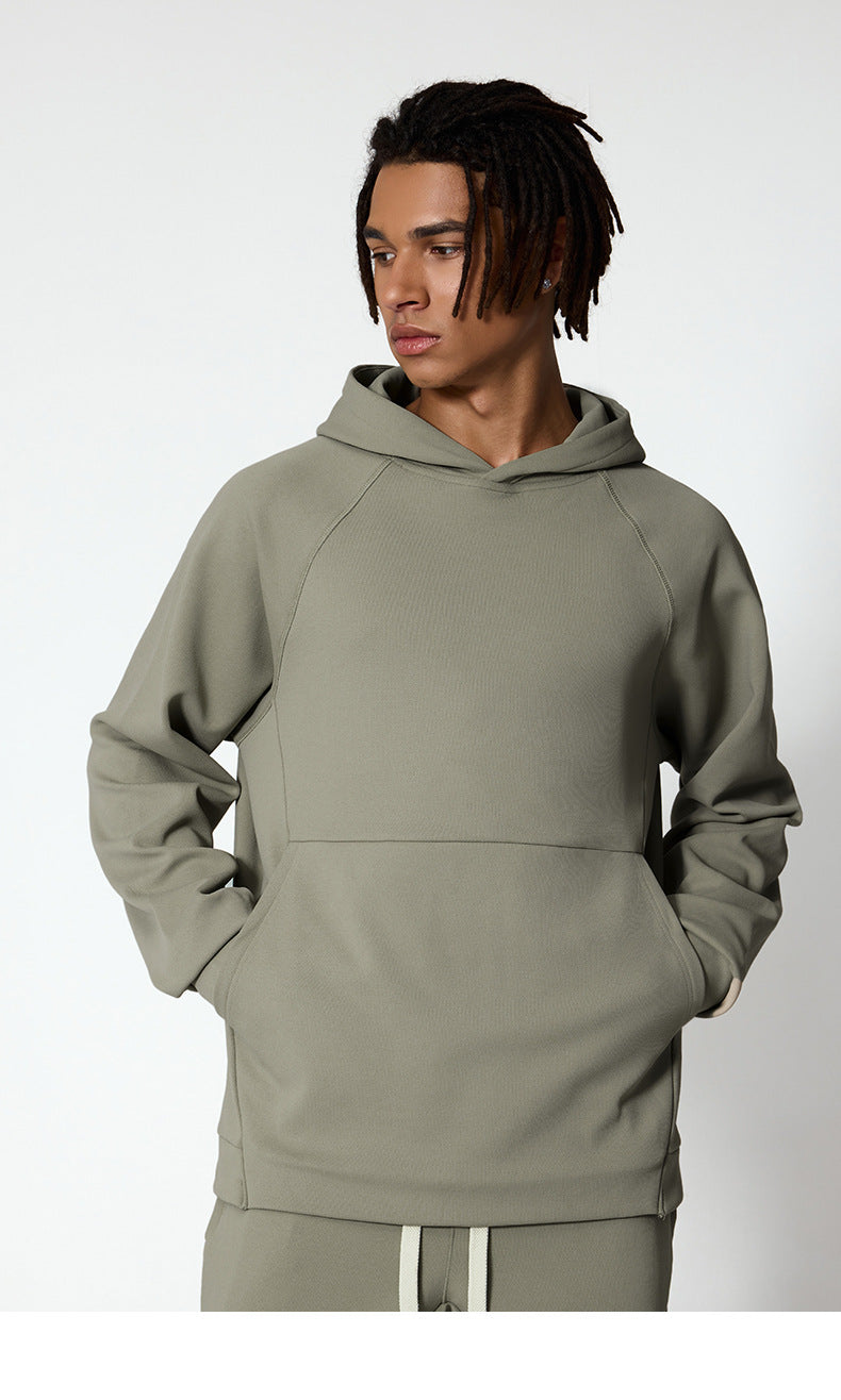 A man is wearing a sage green hoodie with hands in the front pocket, looking to the side