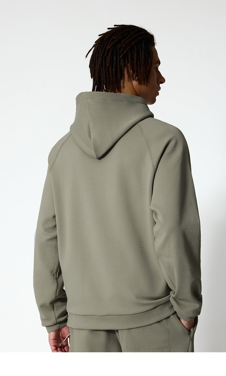A back view of a man wearing a sage green hoodie, showing the hood and relaxed fit