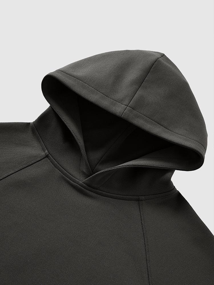 A close-up of a dark gray hoodie’s hood and shoulder seam, laid flat on a light gray background