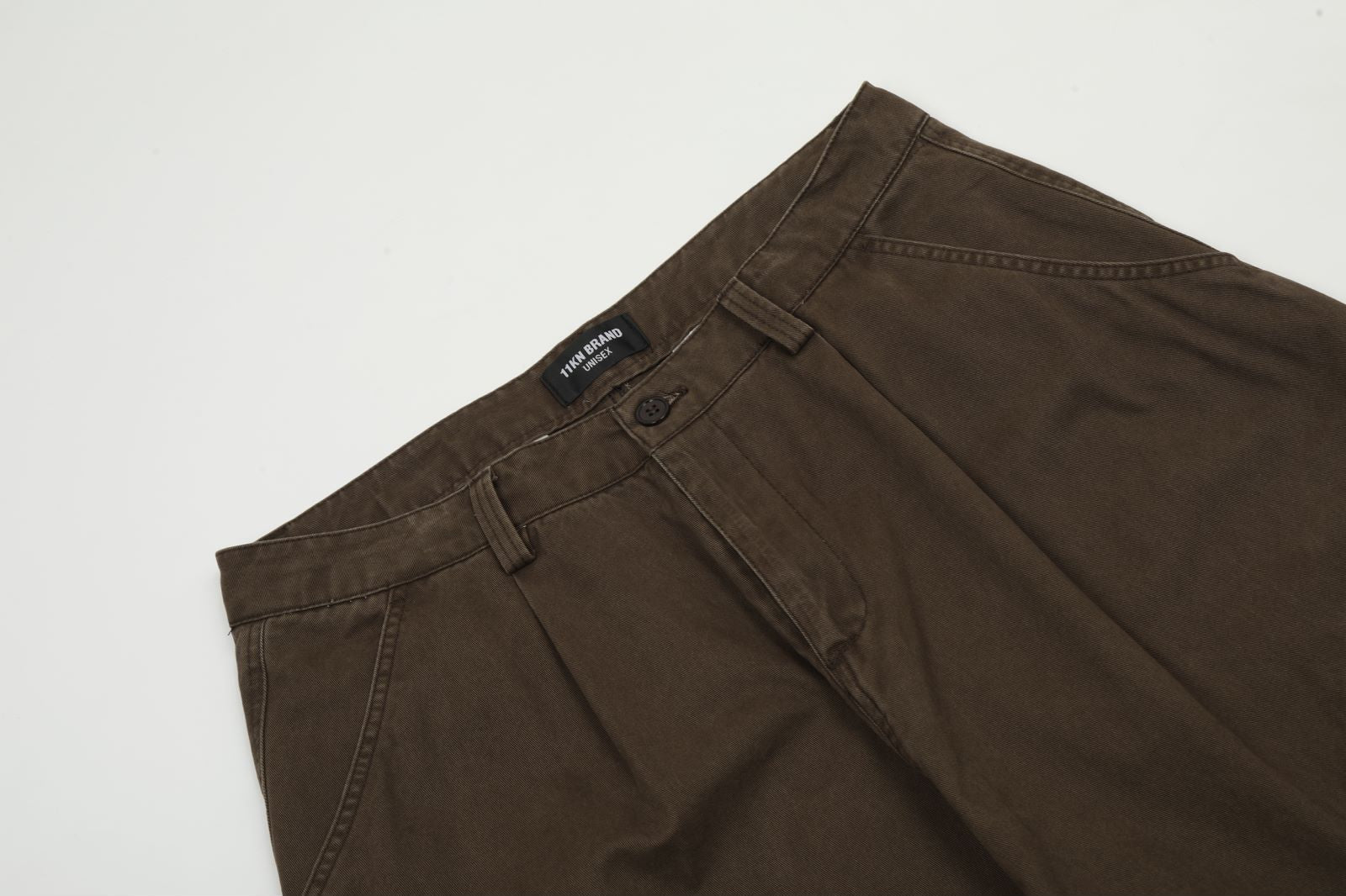 Close-up detail of brown cargo pants waistband showing Titan Brand label and button closure against white background