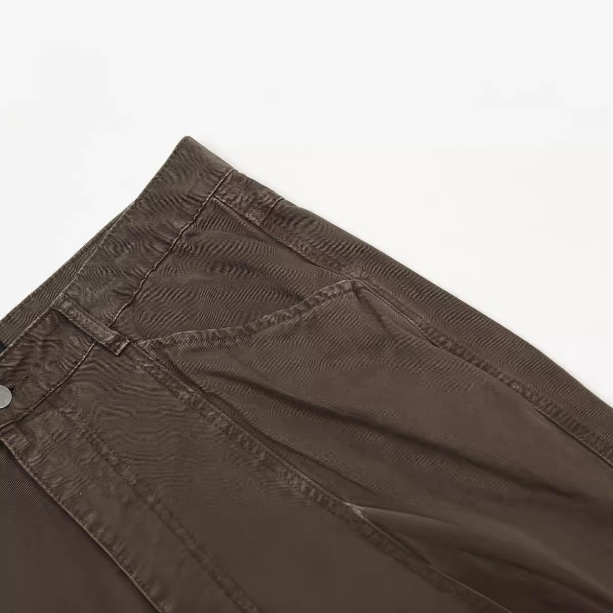 Fabric detail of brown utility pants showing diagonal seam construction and twill texture on white surface