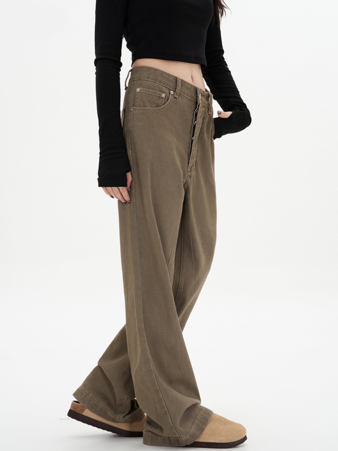A woman wearing olive-brown wide-leg pants with her hand in pocket, black long-sleeve crop top, and beige platform boots shown from side angle