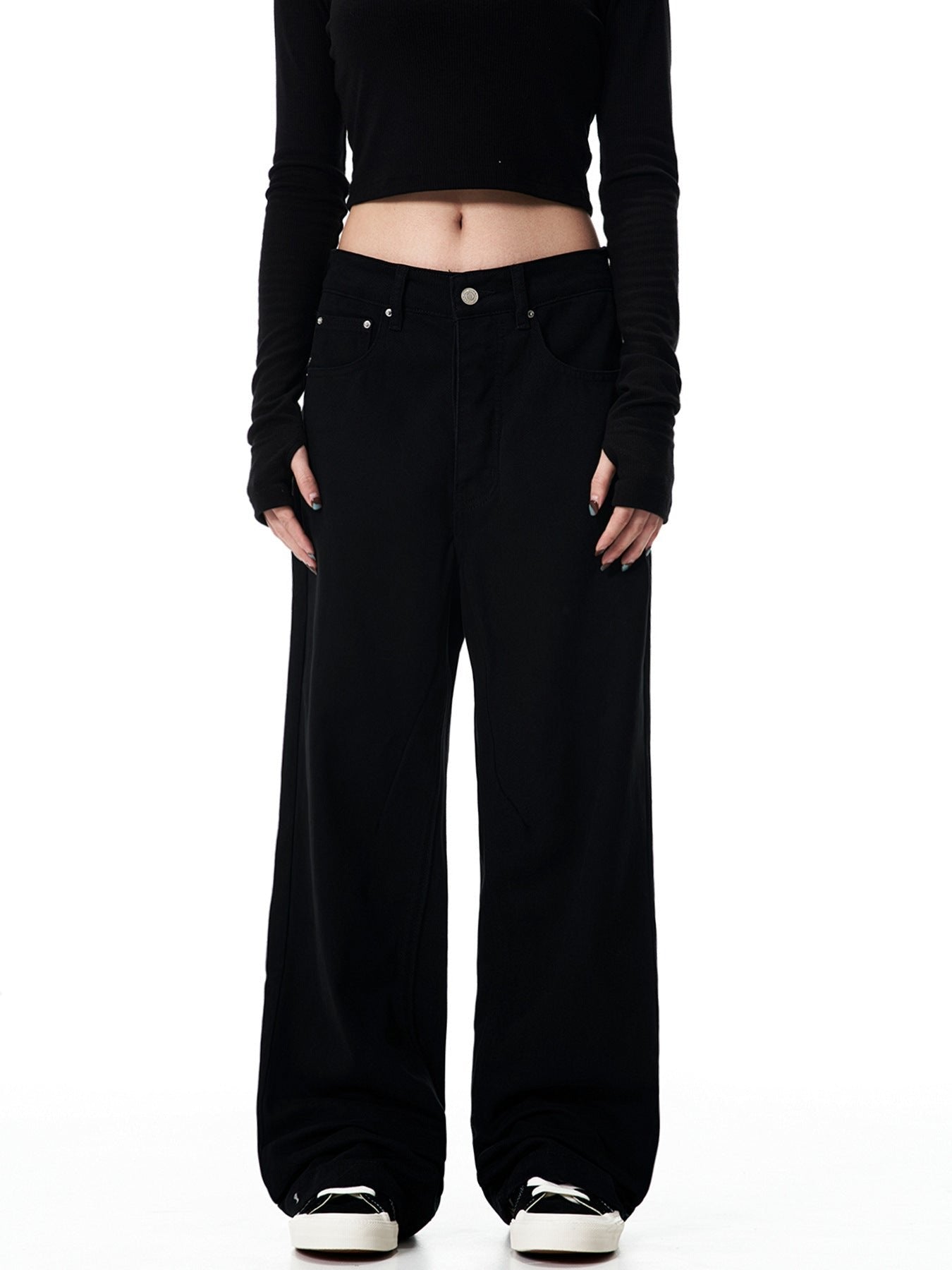 A woman standing in black wide-leg pants with high waist, black long-sleeve crop top, and white sneakers shown from front